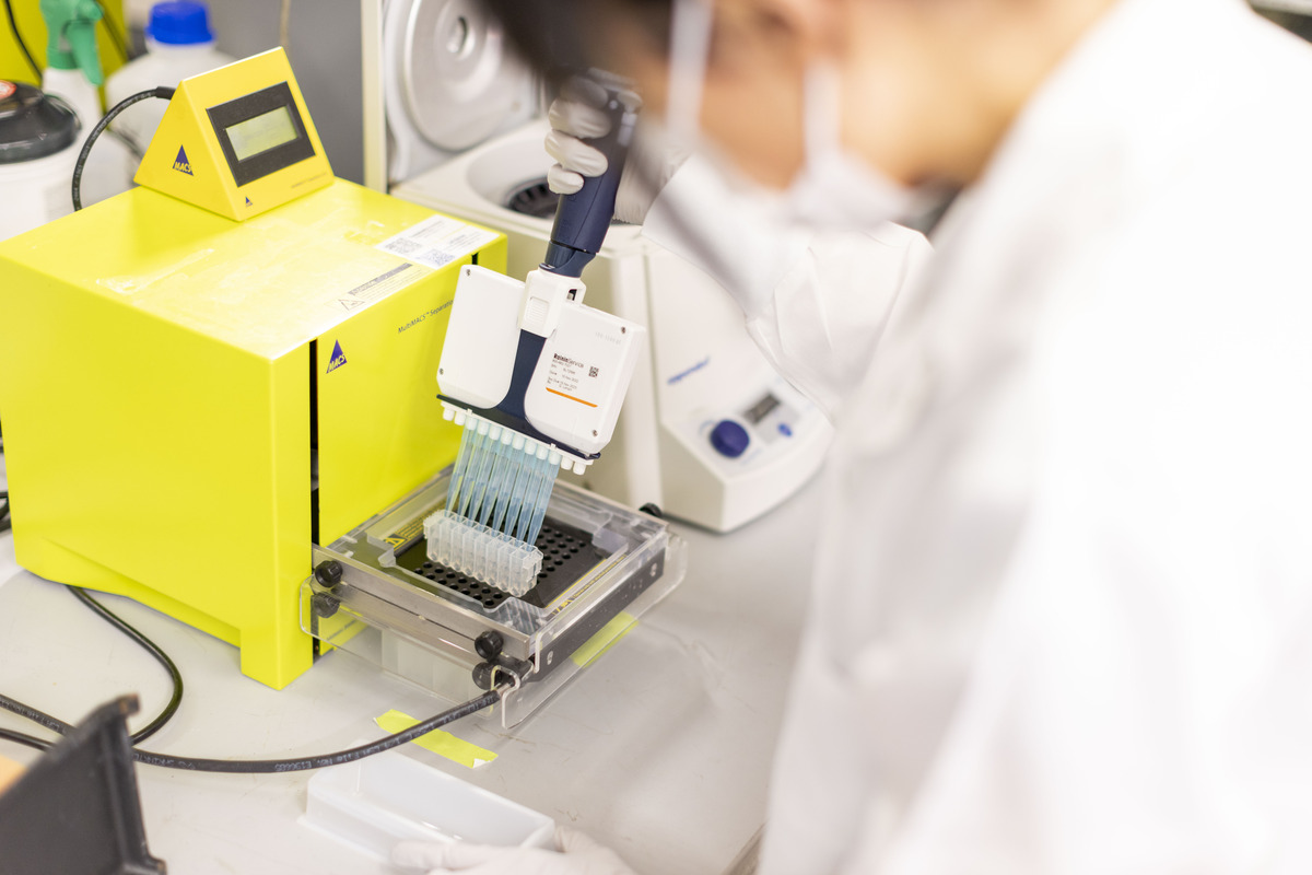 A scientist in a white coat uses a piece of bright yellow lab equipment.