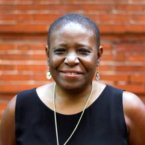 A woman smiles and wears a black blouse and earrings.