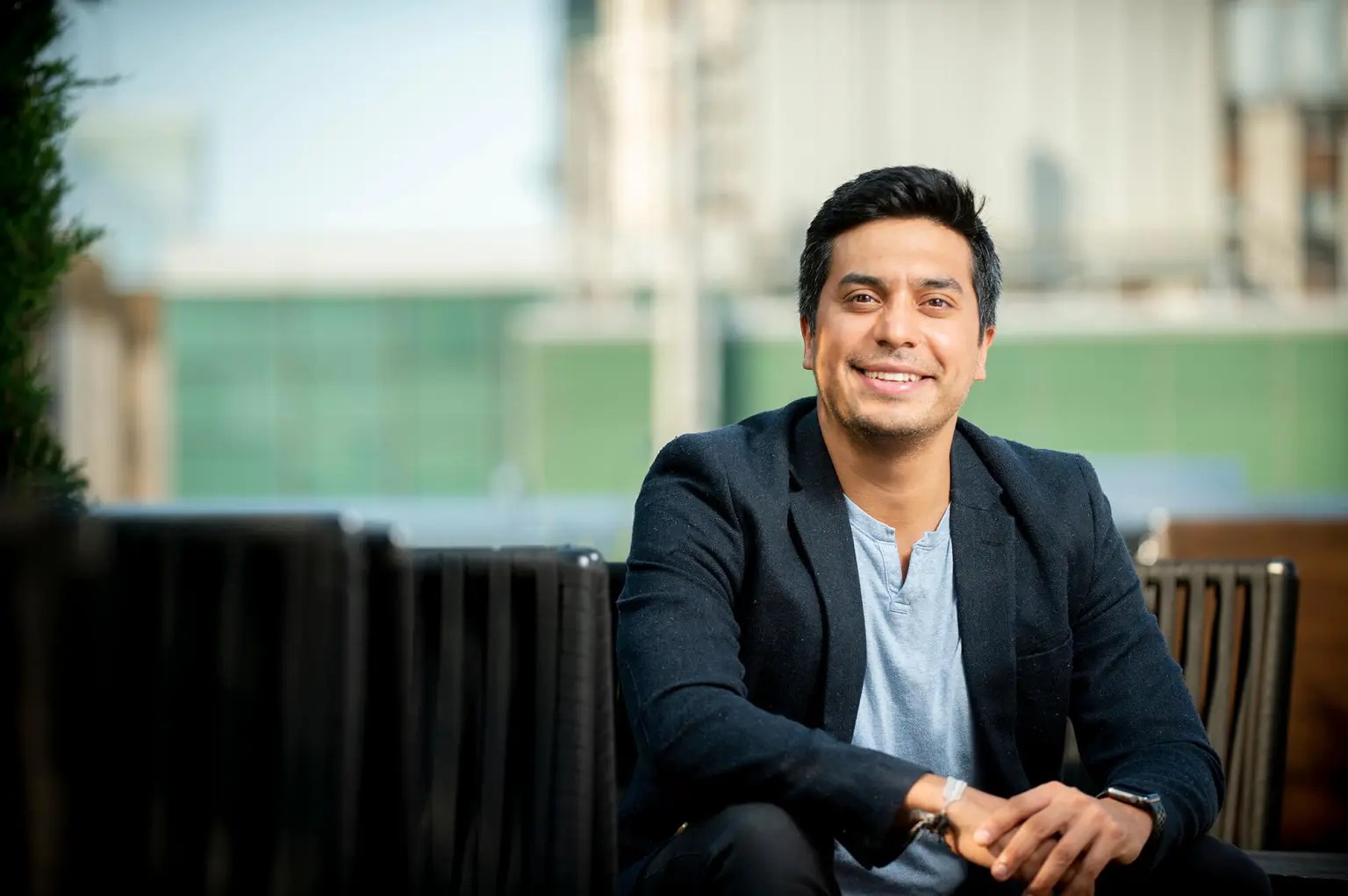 Erick Estrada wears a knit blazer and smiles with his hands clasped.