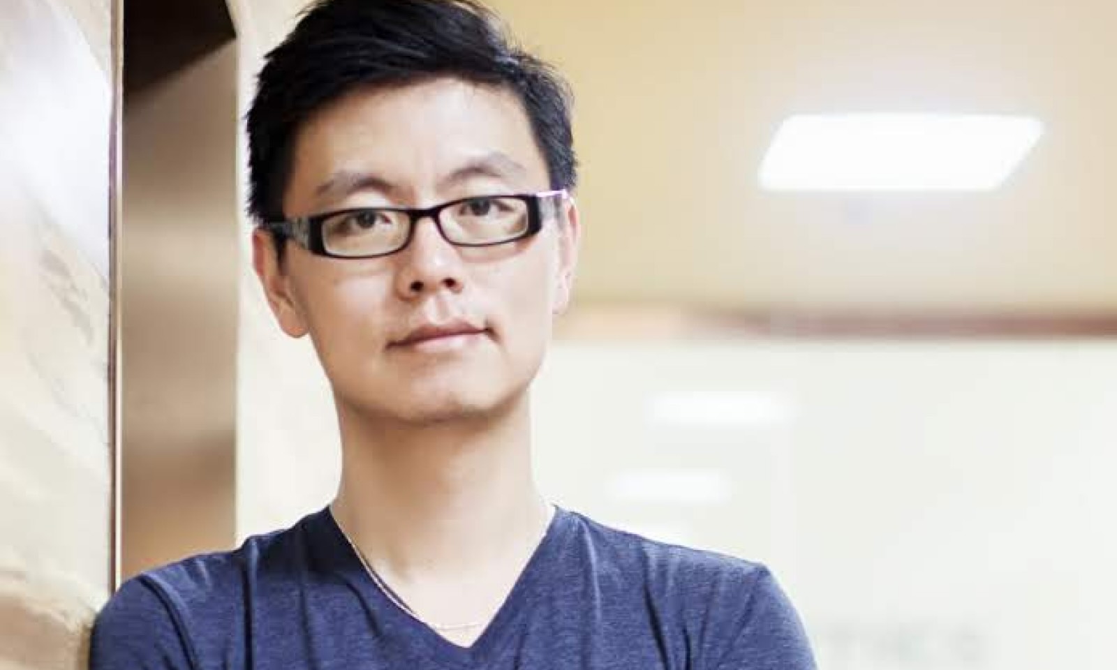 A headshot of a man wearing black glasses and a blue T-shirt.