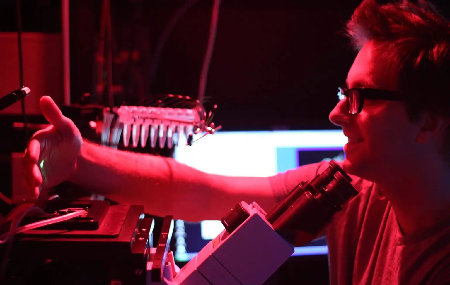 A man works with a microscope in a red-lit room.